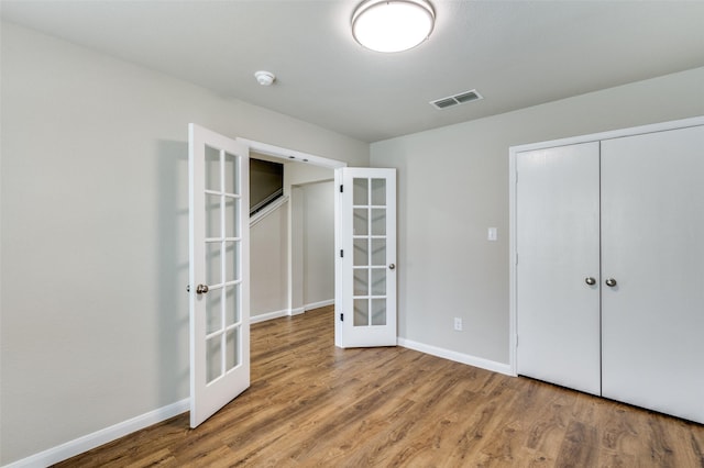 unfurnished bedroom with wood finished floors, visible vents, baseboards, french doors, and a closet