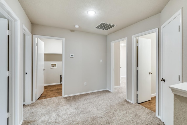 interior space featuring baseboards, a textured ceiling, visible vents, and light colored carpet