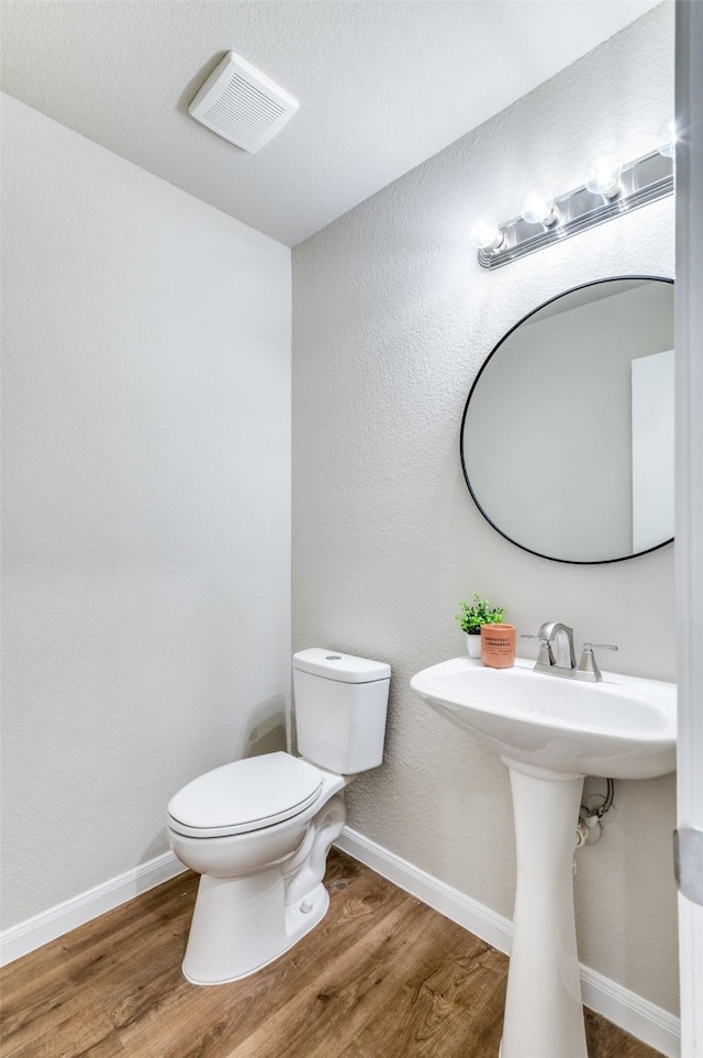 half bathroom featuring baseboards, visible vents, toilet, and wood finished floors