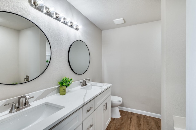 full bath featuring double vanity, a sink, toilet, and wood finished floors