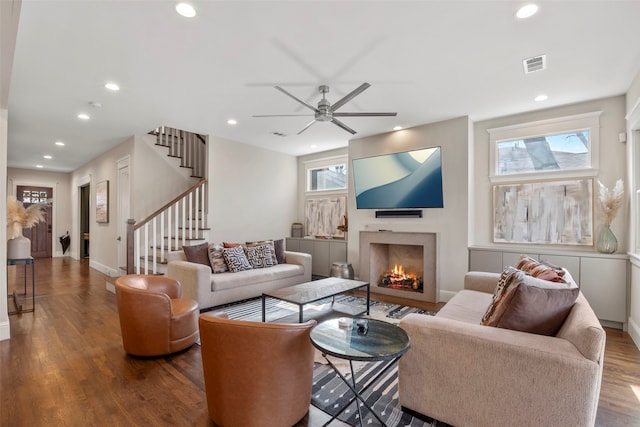 living room featuring visible vents, stairway, dark wood-style flooring, a lit fireplace, and recessed lighting