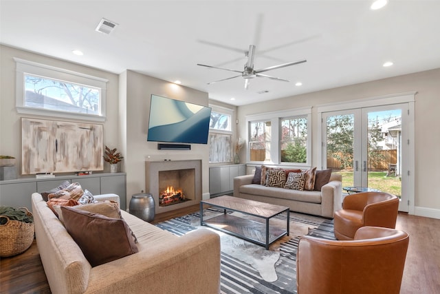 living area featuring french doors, recessed lighting, visible vents, wood finished floors, and a warm lit fireplace