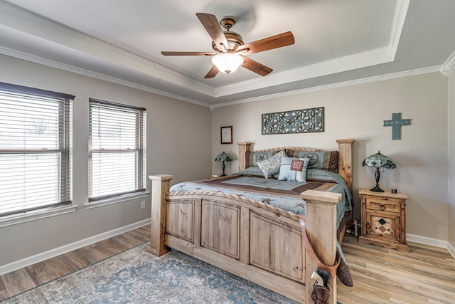 bedroom featuring ornamental molding, a tray ceiling, light wood-type flooring, and baseboards