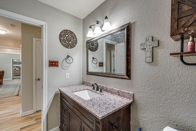 half bathroom with a textured wall, vanity, baseboards, and wood finished floors