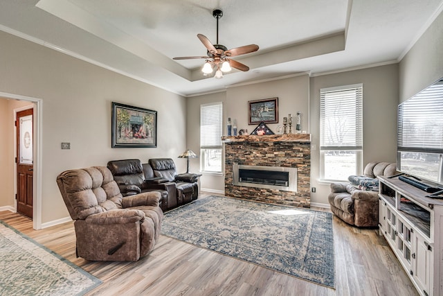 living area with light wood-style flooring, baseboards, a raised ceiling, and a stone fireplace