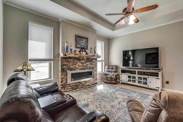 living room with a fireplace, wood finished floors, a ceiling fan, ornamental molding, and a raised ceiling