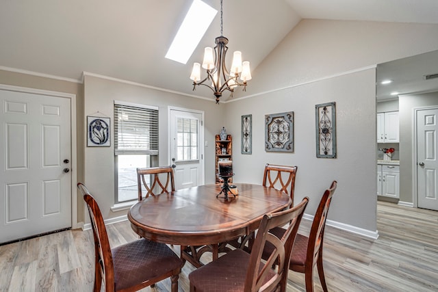 dining area with light wood finished floors, an inviting chandelier, ornamental molding, vaulted ceiling with skylight, and baseboards