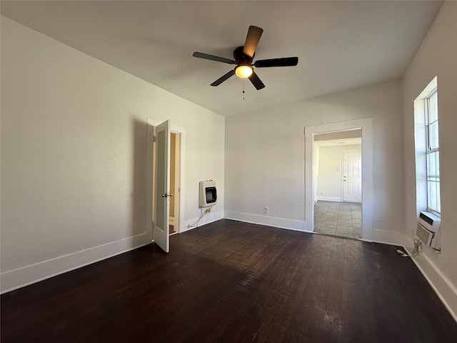 spare room featuring a ceiling fan, dark wood-style flooring, baseboards, and heating unit