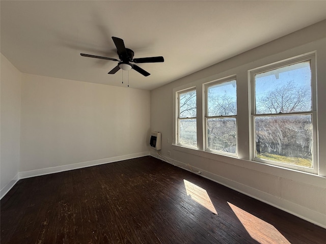 empty room featuring a ceiling fan, heating unit, dark wood finished floors, and baseboards