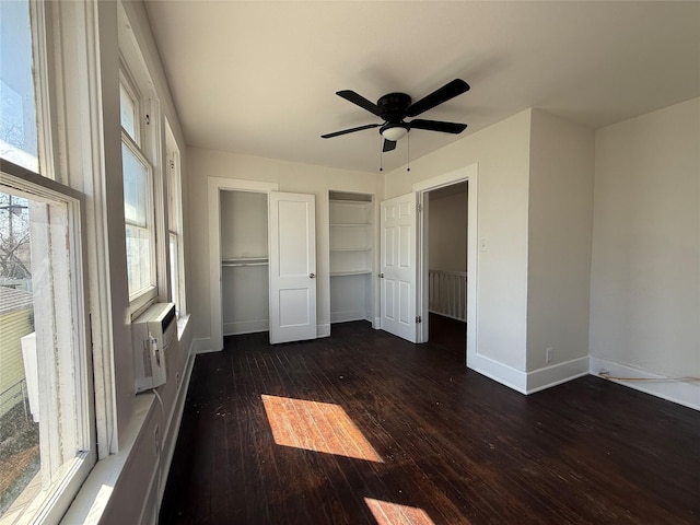 unfurnished bedroom featuring dark wood-style floors, ceiling fan, a wall unit AC, and baseboards