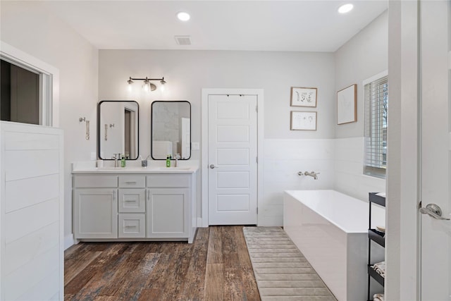 bathroom featuring double vanity, visible vents, wood finished floors, a freestanding bath, and a sink