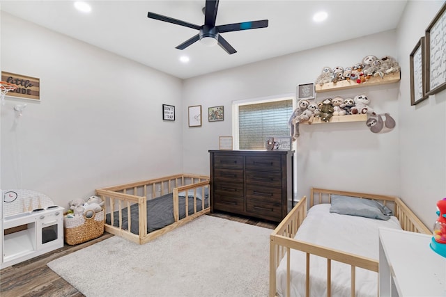 bedroom featuring ceiling fan, a nursery area, wood finished floors, and recessed lighting