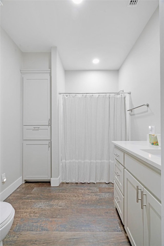 bathroom featuring baseboards, toilet, wood finished floors, shower / bath combo with shower curtain, and vanity