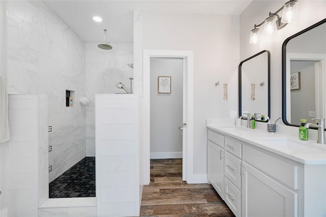 full bath with double vanity, walk in shower, a sink, and wood finished floors