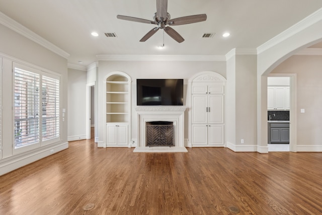 unfurnished living room featuring a fireplace with raised hearth, ornamental molding, wood finished floors, and visible vents