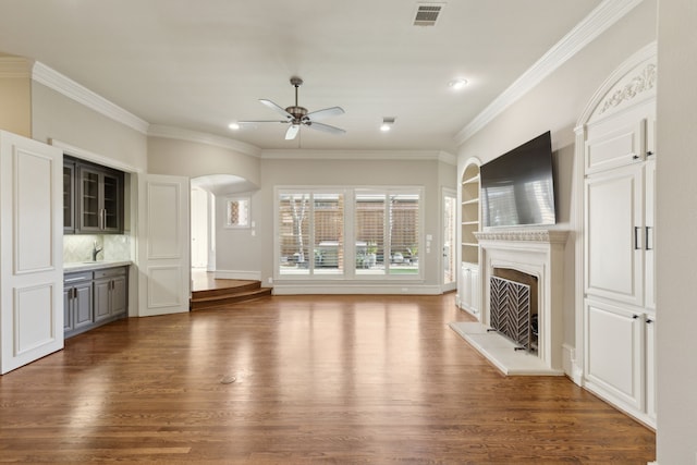 unfurnished living room with a fireplace with raised hearth, dark wood-style floors, visible vents, and arched walkways