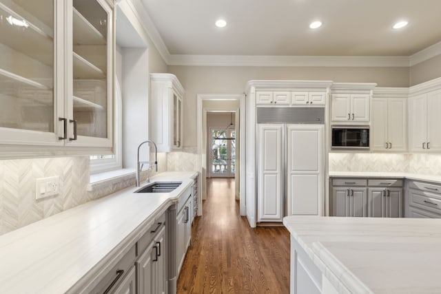 kitchen with dark wood-style flooring, glass insert cabinets, white cabinetry, a sink, and built in appliances