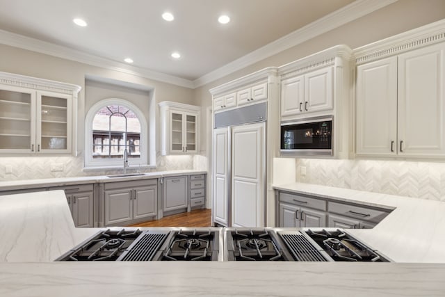 kitchen with glass insert cabinets, ornamental molding, white cabinets, a sink, and built in appliances