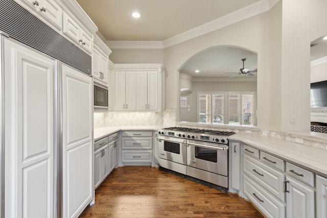 kitchen with dark wood finished floors, crown molding, white cabinetry, built in appliances, and a peninsula