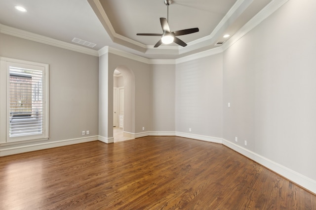 spare room featuring dark wood-style floors, a tray ceiling, arched walkways, crown molding, and visible vents