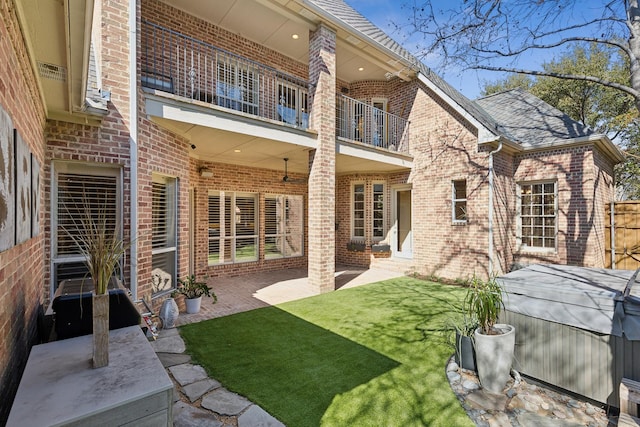 rear view of house featuring roof with shingles, brick siding, a yard, a patio, and a balcony