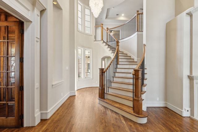 foyer with a notable chandelier, a high ceiling, wood finished floors, baseboards, and stairs