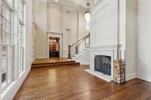 foyer featuring visible vents, a fireplace with raised hearth, dark wood finished floors, a towering ceiling, and ornamental molding