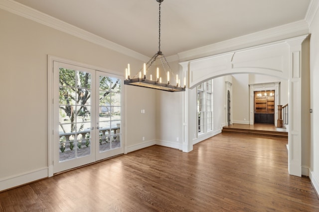 unfurnished dining area featuring arched walkways, wood finished floors, ornamental molding, stairway, and an inviting chandelier