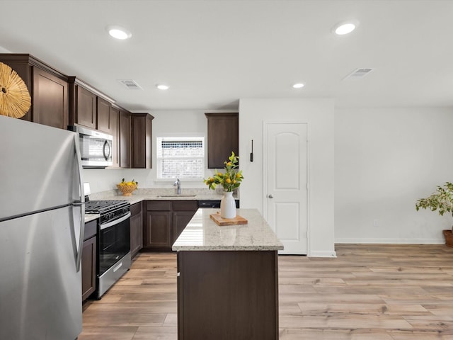 kitchen with light wood finished floors, appliances with stainless steel finishes, light stone counters, a center island, and recessed lighting