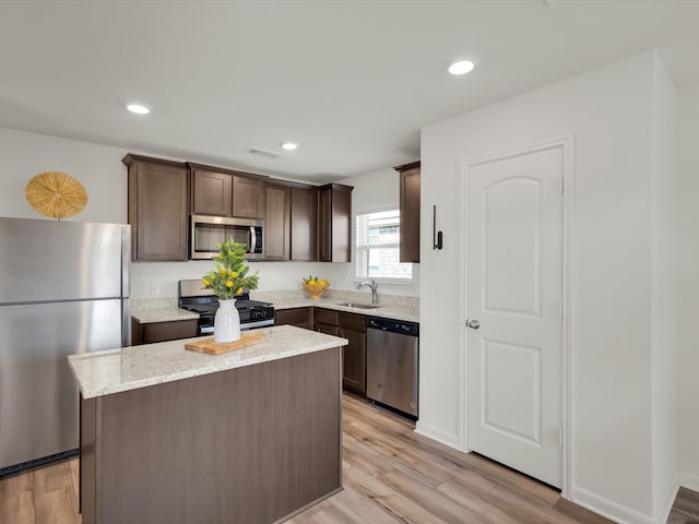 kitchen with stainless steel appliances, light wood-style floors, a sink, a kitchen island, and dark brown cabinets