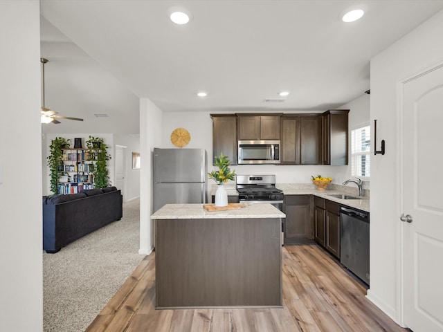 kitchen with dark brown cabinetry, a kitchen island, a sink, open floor plan, and appliances with stainless steel finishes