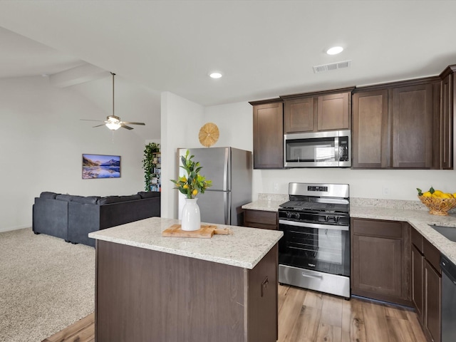 kitchen featuring dark brown cabinetry, visible vents, light stone counters, open floor plan, and stainless steel appliances