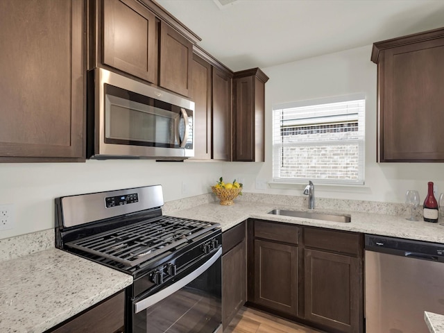 kitchen with light stone countertops, dark brown cabinets, stainless steel appliances, and a sink