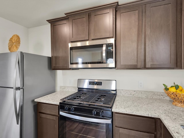 kitchen featuring dark brown cabinets, appliances with stainless steel finishes, and light stone counters