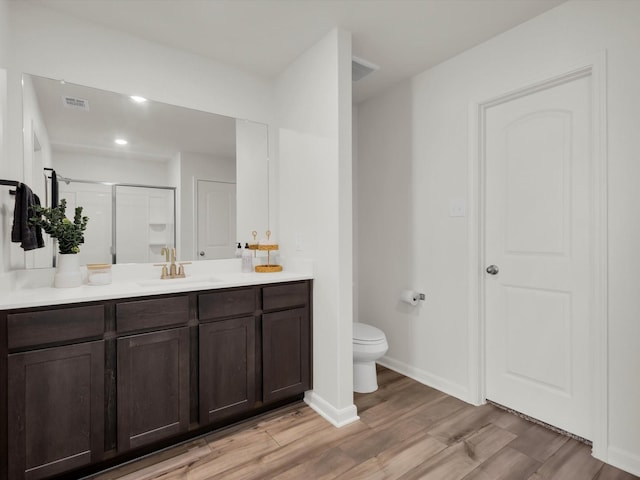 bathroom with visible vents, toilet, wood finished floors, vanity, and a shower stall