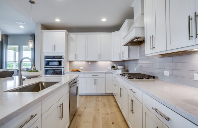 kitchen featuring stainless steel appliances, a sink, hanging light fixtures, custom exhaust hood, and light stone countertops