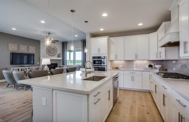 kitchen with hanging light fixtures, appliances with stainless steel finishes, white cabinetry, a sink, and an island with sink