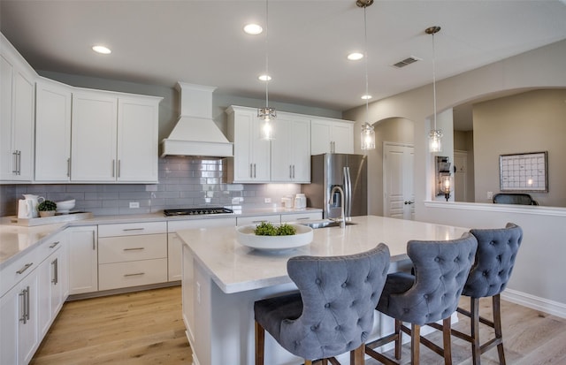 kitchen with decorative light fixtures, stainless steel refrigerator with ice dispenser, visible vents, custom range hood, and an island with sink