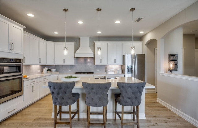 kitchen featuring white cabinets, appliances with stainless steel finishes, decorative light fixtures, custom exhaust hood, and light countertops