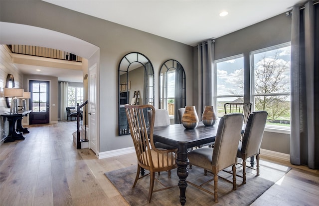 dining area with arched walkways, recessed lighting, stairway, light wood-style floors, and baseboards