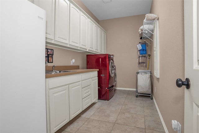 clothes washing area featuring light tile patterned floors, a sink, baseboards, separate washer and dryer, and cabinet space