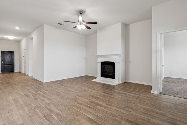 unfurnished living room with ceiling fan, light wood-type flooring, a glass covered fireplace, and visible vents