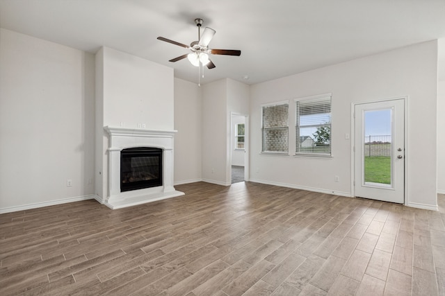 unfurnished living room with a glass covered fireplace, baseboards, ceiling fan, and light wood finished floors