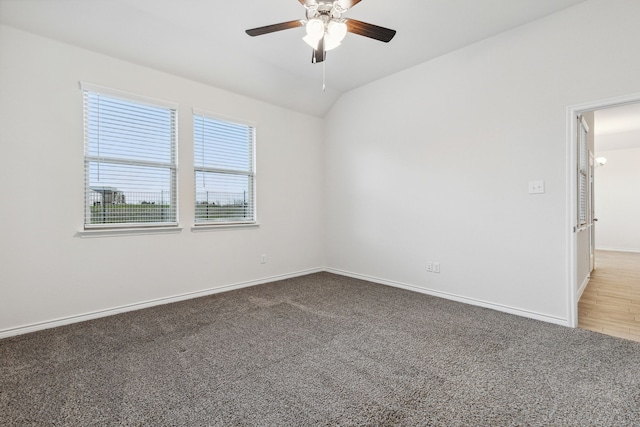 empty room featuring lofted ceiling, carpet, baseboards, and a ceiling fan