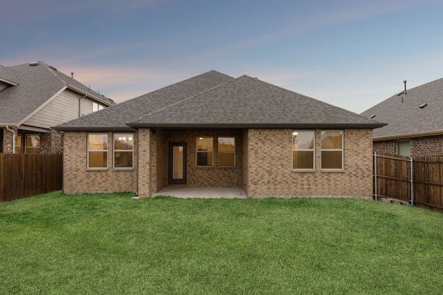 rear view of property featuring a shingled roof, a yard, a fenced backyard, and a patio