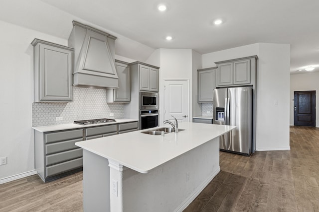 kitchen featuring a center island with sink, appliances with stainless steel finishes, gray cabinets, light countertops, and a sink