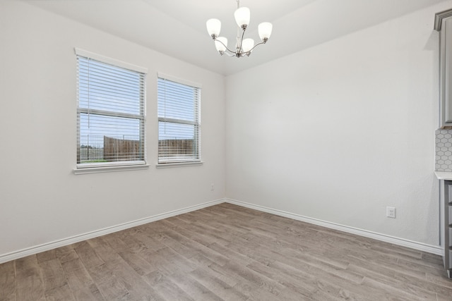 unfurnished dining area featuring baseboards, light wood-style flooring, and an inviting chandelier