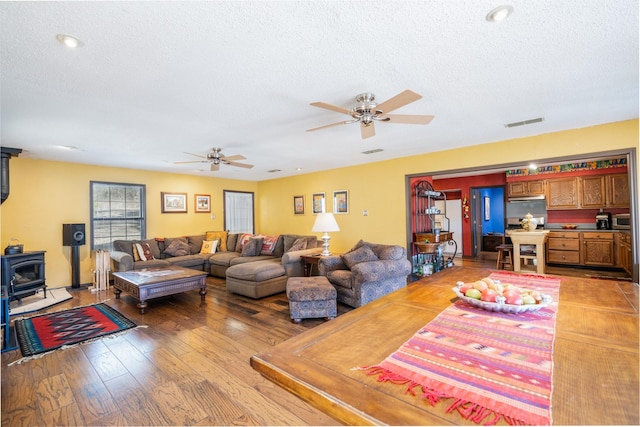 living room featuring a wood stove, light wood-style flooring, visible vents, and a textured ceiling