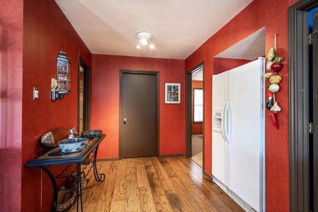 corridor with light wood-type flooring and a textured ceiling