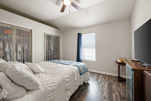 bedroom with two closets, baseboards, vaulted ceiling, a ceiling fan, and dark wood-style flooring